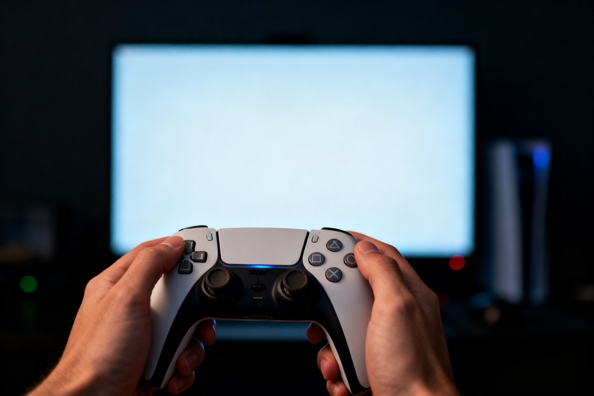 Mains tenant une manette devant l'écran lumineux d'un ordinateur dans une pièce sombre