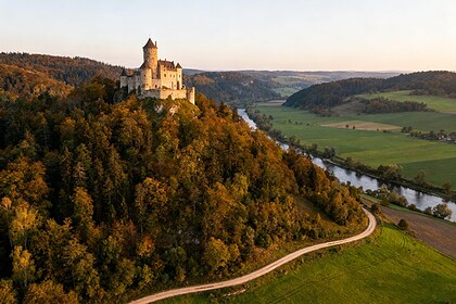 Château médiéval en pierre sur une colline boisée dominant une vallée et une rivière
