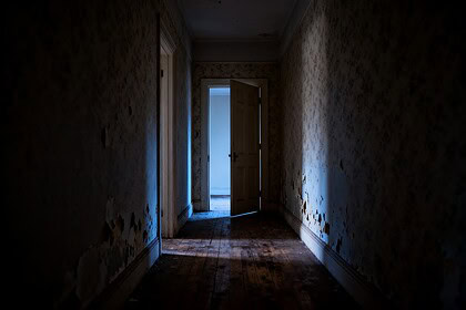Couloir sombre d'un appartement ancien avec une porte entrouverte au fond