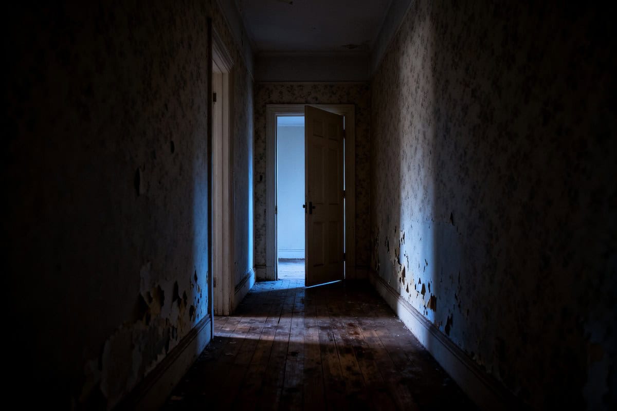 Couloir sombre d'un appartement ancien avec une porte entrouverte au fond