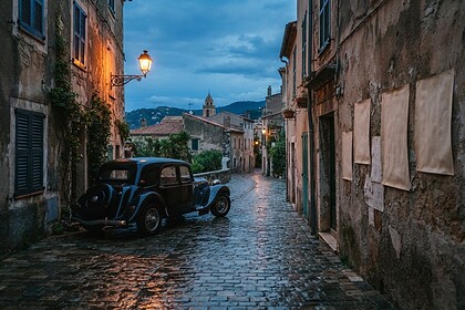 Berline noire ancienne garée dans une ruelle pavée et mouillée d'un village méditerranéen au crépuscule