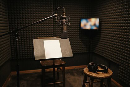 Micro de studio sur perche dans une cabine d'enregistrement sombre, casque posé sur un tabouret et chaise vide