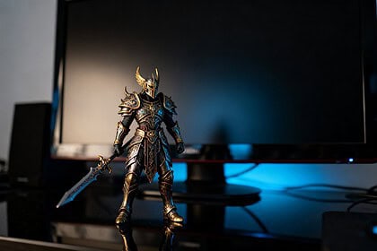 Figurine de guerrier fantasy en armure dorée posée sur un bureau sombre devant un écran éteint