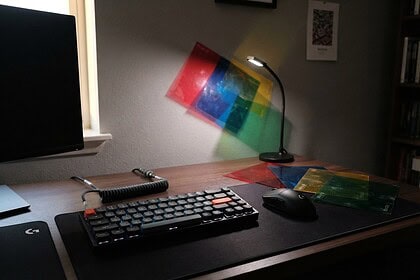 Clavier de jeu et filtres colorés sur un bureau, projetant des carrés rouges, bleus et verts sur un mur gris