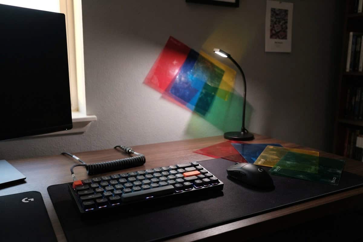 Clavier de jeu et filtres colorés sur un bureau, projetant des carrés rouges, bleus et verts sur un mur gris