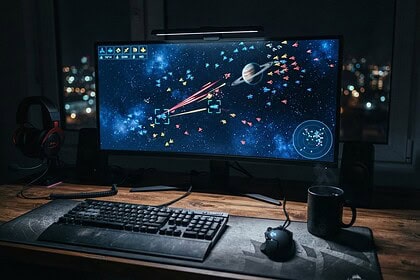 Écran d'ordinateur affichant un jeu de stratégie spatiale en vue de dessus, sur un bureau la nuit