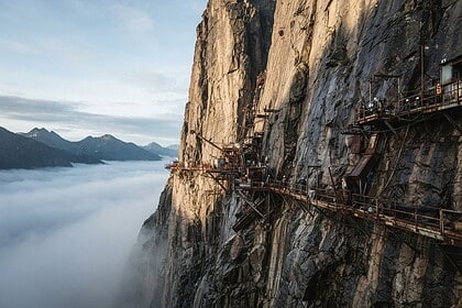 Falaise vertigineuse émergeant des nuages, plateformes et treuils miniers accrochés à la paroi