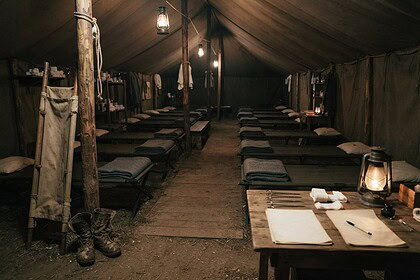 Intérieur d'une tente-hôpital de campagne éclairée aux lampes à pétrole, lits de camp alignés