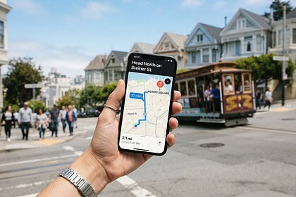 Main tenant un smartphone affichant une application de navigation, devant des maisons victoriennes de San Francisco
