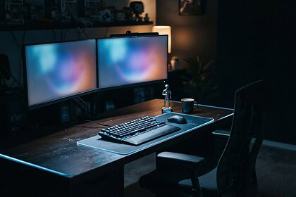 Bureau de jeu inoccupé la nuit, clavier mécanique rétroéclairé, souris et deux écrans aux couleurs floues