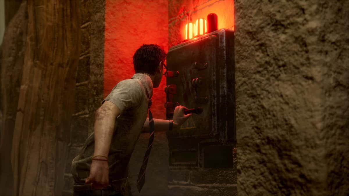 Un survivant blessé actionne un générateur surmonté de voyants rouges dans un couloir de pierre