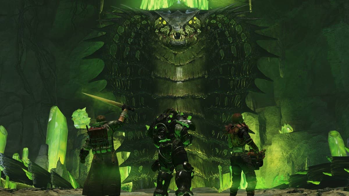 Trois joueurs, dont un en armure assistée, face à une immense créature dans une grotte aux cristaux verts