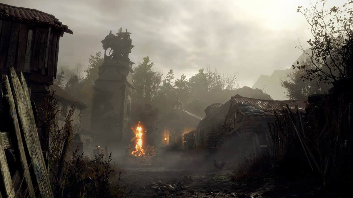 Rue boueuse d'un village rural sous la brume, avec un bûcher en flammes devant une tour de pierre et des maisons délabrées