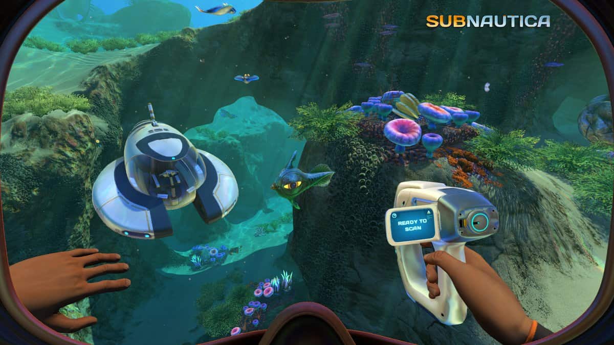 Vue à la première personne d'un plongeur tenant un scanner devant un petit submersible blanc, près d'un récif coloré